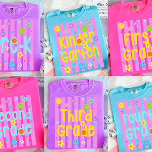 May include: A collection of colorful t-shirts, each displaying a grade level: Pre-K, Kindergarten, First Grade, Second Grade, Third Grade, and Fourth Grade. The shirts feature a striped design with smiley faces and flowers.
