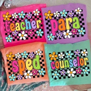 May include: Four colorful t-shirts with floral designs and the words "teacher", "para", "sped", and "counselor". Each shirt has a different background color: pink, purple, orange, and teal. The text is in a retro font with a checkerboard pattern.