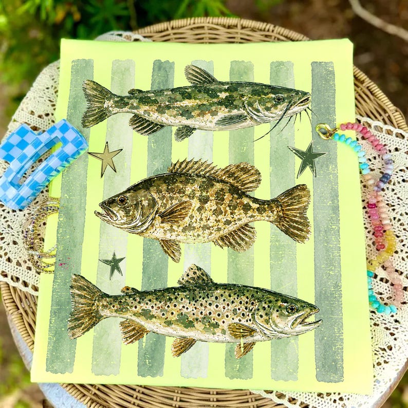 May include: A canvas print featuring three detailed illustrations of fish: a catfish, a bass, and a trout. The background is a bright yellow-green with vertical stripes. Decorative stars and jewelry are placed around the canvas.