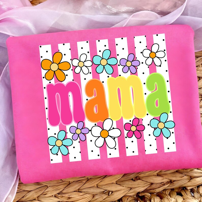 May include: A pink t-shirt with the word "mama" in colorful, bubble letters. The shirt features a white and black striped design with colorful flowers. The flowers are orange, white, blue, purple, and pink.