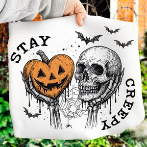 May include: White Halloween-themed tote bag with a pumpkin-shaped jack-o'-lantern and a skull. The words "STAY CREEPY" are printed on the bag. Bats and a spiderweb are also featured in the design.