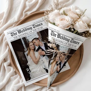 Op de afbeelding: Een trouw-thema krant met de kop "The Wedding Times" en de datum 8 augustus 2027. De krant toont een foto van een stel en de tekst "Emily & Will Say I Do". Een boeket witte rozen is verpakt in een krantenkegel.