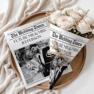 Op de afbeelding: Een boeket crèmekleurige rozen verpakt in een krantachtige kegel, met de kop "The Wedding Times" en de namen "Future Mr & Mrs Jefferson". Een bijpassende krant is ook zichtbaar.