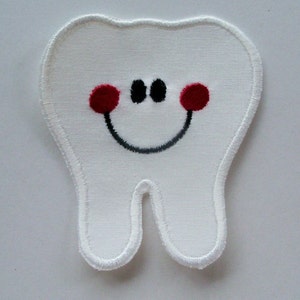 May include: A white embroidered tooth-shaped patch with a smiling face. The tooth features red cheeks, black eyes, and a black curved mouth. The patch is made of a textured fabric with a white border.