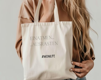 Könnte beinhalten: Eine weiße Stofftasche mit schwarzem Text, der "Einatmen... ...Ausrasten #MOMLIFE" lautet.