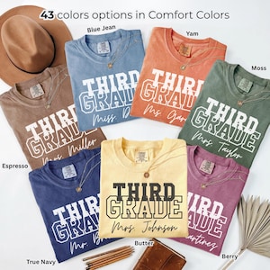 May include: A collection of seven short-sleeved t-shirts in various colors including blue jean, yam, moss, espresso, true navy, butter, and berry. Each shirt features the text THIRD GRADE in a collegiate font and a personalized name below.