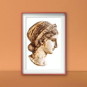Puede incluir: Impresión enmarcada de un busto clásico de perfil. El busto es de color beige claro con rasgos faciales detallados y un tocado. El marco es de color rojo claro y el fondo es blanco.