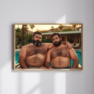 May include: A framed print featuring two shirtless men with dark beards, sitting side-by-side. One man has his arm around the other's shoulder. The background shows a swimming pool, palm trees, and a sunset.