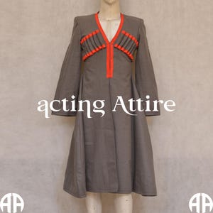 May include: A gray long-sleeved coat with a red and black trim around the neckline and down the front. The coat has a V-neck and a flared skirt.