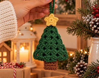 May include: A dark green crochet Christmas tree ornament featuring a yellow star at the top and a brown rectangular trunk at the base. The tree has a textured, open-stitch pattern and includes a matching green loop for hanging.