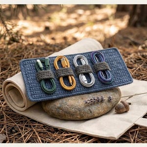May include: A blue rectangular crochet cable organizer featuring four dark grey crocheted loops holding green, yellow, white, and purple charging cables. The text CROCHET CABLE ORGANIZER and INSTANT DOWNLOAD HIGH QUALITY is visible at the top and bottom.