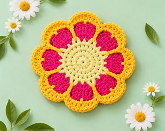 Può includere: Un sottobicchiere all'uncinetto a forma di fiore con un centro giallo pallido, petali fucsia vivaci e un bordo smerlato giallo brillante. L'oggetto in tessuto è circondato da diverse margherite bianche con foglie verdi.