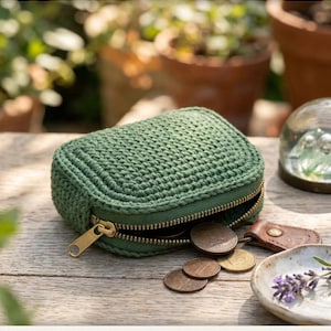 Può includere: Un portamonete all'uncinetto color verde salvia con chiusura a zip in metallo dorato. Il portamonete è parzialmente aperto e rivela diverse monete metalliche sulla superficie. È presente il testo CROCHET COIN PURSE, INSTANT DOWNLOAD, HIGH QUALITY.