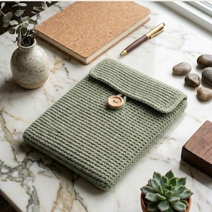 May include: A sage green crochet Kindle cover featuring a rectangular shape with a fold-over flap secured by a single light brown wooden button. The cover has a textured, ribbed stitch pattern and is presented as a digital item for download.