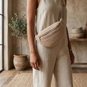 Peut inclure: Un sac banane en crochet beige présentant un motif tissé texturé avec une fermeture éclair horizontale sur le dessus. Le sac est fixé à une sangle réglable beige assortie, conçue pour être portée en travers de la poitrine ou à la taille.