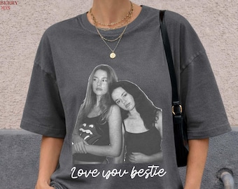 May include: Dark gray t-shirt featuring a black and white image of two women with the text "love you bestie". The shirt has short sleeves and a relaxed fit. The brand logo "Moonberry Goods" is visible in the upper left corner.