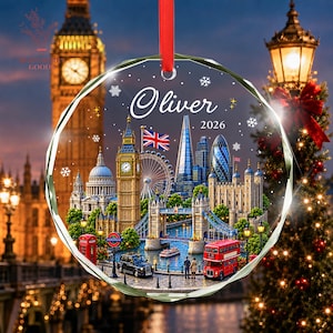 May include: A round, clear glass ornament featuring a printed illustration of London landmarks including Big Ben, Tower Bridge, and the London Eye. The text "Oliver" and "2026" is printed in white, accompanied by snowflake graphics and a red ribbon.