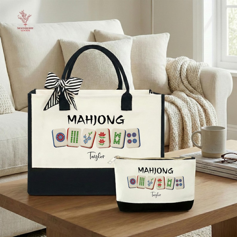 May include: A canvas tote bag and matching zippered pouch, both featuring the word "MAHJONG" and colorful tile illustrations. The tote has black handles and a black and white striped bow. The bottom of both items is black.
