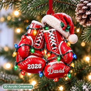 May include: A pair of red boxing gloves hanging as a Christmas ornament, featuring a Santa hat on top, wrapped in colorful string lights. The left glove displays the year 2026 in white, and the right glove features the name David in white script.