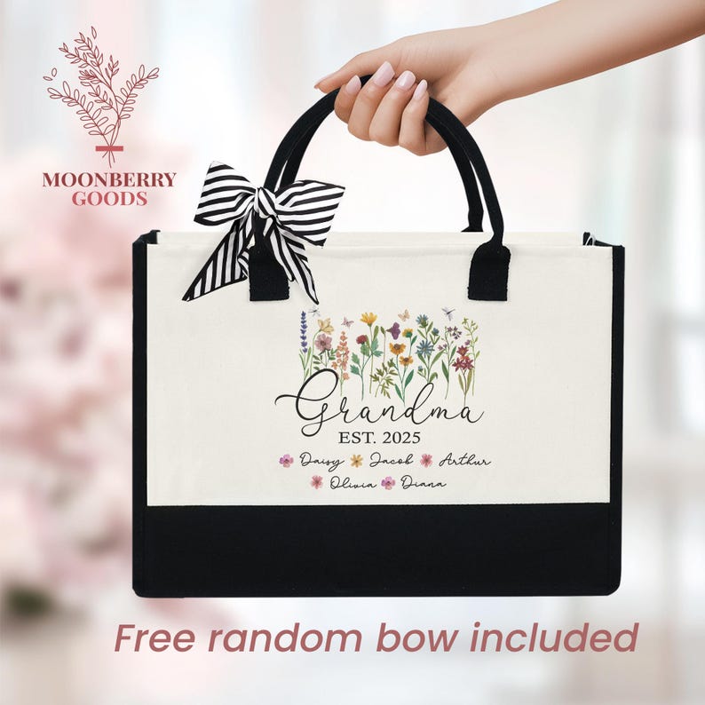 May include: A white canvas tote bag with black trim and handles. The bag features a floral design with the text "Grandma Est. 2025" and the names "Daisy, Jacob, Arthur, Olivia, Diana".