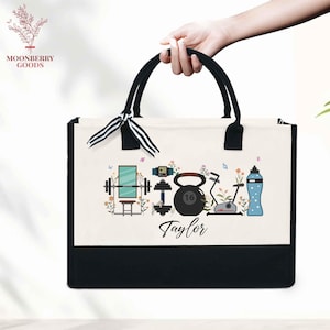 May include: A canvas tote bag with black handles and a black bottom. The bag features a fitness-themed design with a barbell, kettlebell, exercise bike, and water bottle. The name "Taylor" is printed below the design.