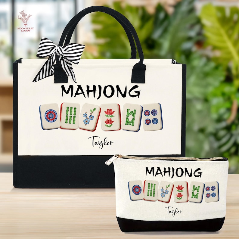 May include: A white tote bag and matching zippered pouch with a black base. Both feature the word "MAHJONG" above colorful Mahjong tiles. The tote has black handles and a striped bow. The name "Taylor" is printed below the tiles.