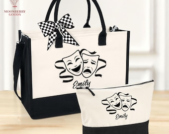 May include: A canvas tote bag and matching cosmetic bag set. The bags are off-white with black accents and handles. Each bag features a black graphic of comedy and tragedy masks with the name "Emily" below. A black and white checkered bow adorns the tote.