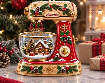 May include: A decorative stand mixer ornament featuring a red and wood-grain finish with holly, pinecone, and snowflake accents. The mixing bowl contains a miniature winter scene with a house, Christmas tree, and snowman. The name Amanda is printed.