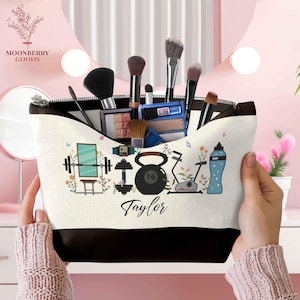 May include: A white and black makeup bag with a zipper, filled with makeup brushes and products. The bag features a fitness-themed design with a barbell, kettlebell, exercise bike, and water bottle. The name "Taylor" is printed on the bag.