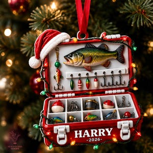 May include: A red tackle box Christmas ornament featuring a Santa hat, a green and yellow fish, and various fishing lures. The box is decorated with a string of colorful lights and displays the name HARRY and the year 2026 on the front exterior.