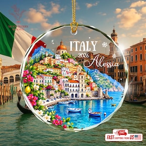 May include: A circular glass ornament featuring a vibrant coastal Italian town scene with colourful buildings, blue water, small boats, and pink flowers. The text ITALY 2026 Alessia is printed in white. It hangs from a gold cord against a background.
