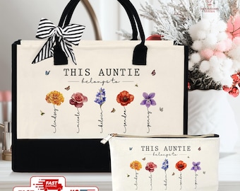 May include: A canvas tote bag and matching cosmetic bag. Both are off-white with black bottoms and handles. The bags feature the text "THIS AUNTIE belongs to" with floral and butterfly designs, and names below the flowers.