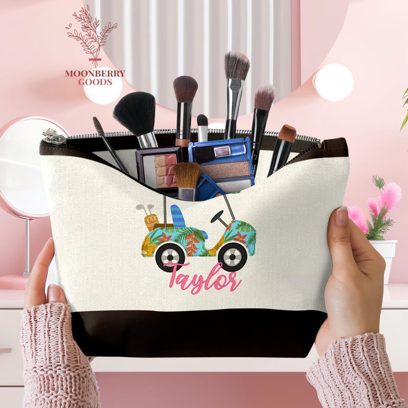 Op de afbeelding: Een witte en zwarte make-uptas met een golfkar-ontwerp in blauw, geel en groen, met de naam "Taylor" in roze script. De tas is gevuld met make-upborstels en -producten.