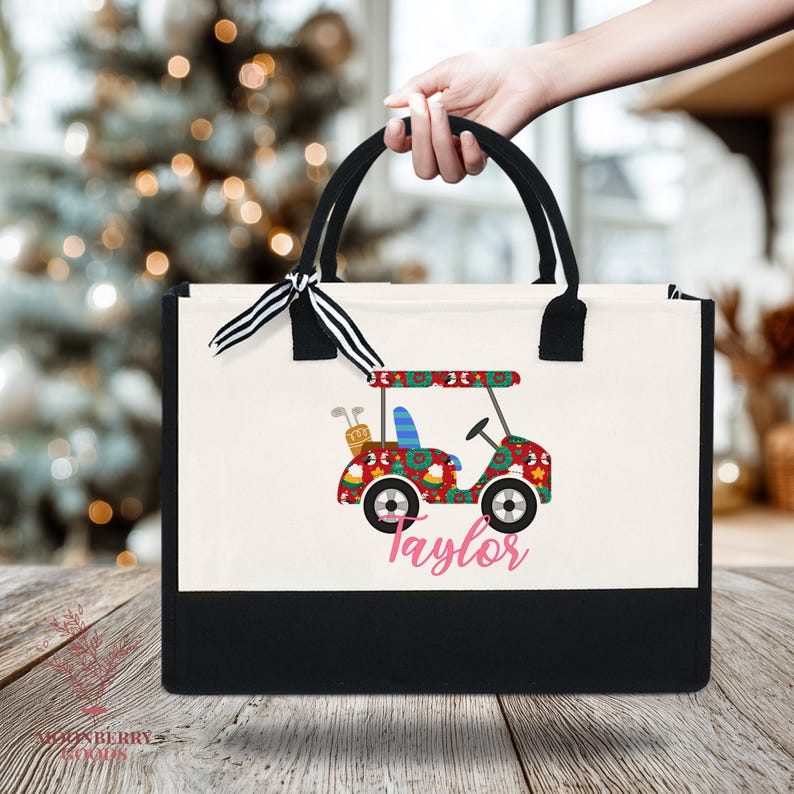 Op de afbeelding: Een canvas draagtas met zwarte handvatten en een zwarte basis. De tas heeft een kleurrijk golfkarretje ontwerp met de naam "Taylor" in roze. Een zwart-wit gestreept lint is aan het handvat geknoopt.