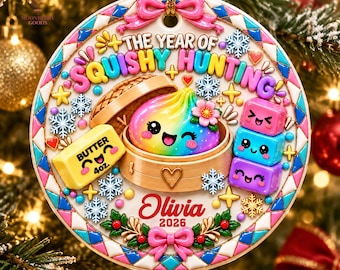 May include: A round 3D relief ceramic ornament featuring a rainbow-coloured dumpling in a bamboo steamer, a yellow butter block labelled 'BUTTER 4oz.', and three stacked colourful cubes. The text reads 'THE YEAR OF SQUISHY HUNTING', 'Olivia', and '2026'.
