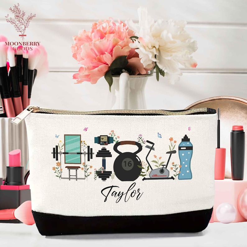 May include: A white canvas cosmetic bag with a black bottom and gold zipper. The bag features a fitness-themed design with a mirror, dumbbells, kettlebell, exercise bike, and water bottle. The name "Taylor" is written on the bag.