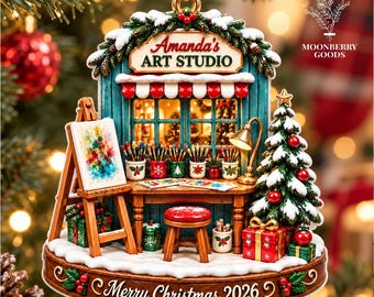 May include: A decorative Christmas ornament featuring a miniature art studio scene with a sign reading Amanda's Art Studio. The piece includes an easel, a desk with paintbrushes, a stool, and a Christmas tree. The base is inscribed with Merry Christmas 2026.
