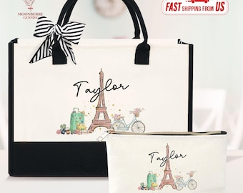 May include: A white tote bag and matching cosmetic bag with black accents. Both bags feature a design with the Eiffel Tower, a bicycle, and the name "Taylor". The tote bag has black handles and a striped bow.