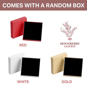 May include: Three square gift boxes with lids, each featuring a black interior. The boxes are available in red, white, and gold colours. The text "COMES WITH A RANDOM BOX" appears at the top, and the logo "MOONBERRY GOODS" is displayed on the right.
