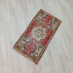 May include: A small, red, beige, and cream colored vintage Turkish rug with a geometric pattern. The rug has a central medallion and a border.