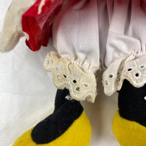 K&ouml;nnte beinhalten: Nahaufnahme einer Minnie Mouse-Puppe. Die Puppe hat schwarze Beine und gelbe Schuhe. Die Puppe tr&auml;gt wei&szlig;e Pumphosen mit Spitzenbesatz und ein rotes Kleid mit wei&szlig;en Punkten.