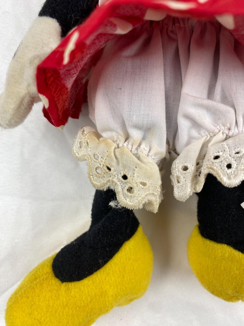 K&ouml;nnte beinhalten: Nahaufnahme einer Minnie Mouse-Puppe. Die Puppe hat schwarze Beine und gelbe Schuhe. Die Puppe tr&auml;gt wei&szlig;e Pumphosen mit Spitzenbesatz und ein rotes Kleid mit wei&szlig;en Punkten.