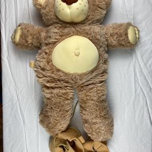 May include: A brown teddy bear with a light brown nose and yellow fur on its belly. The bear is wearing brown boots.