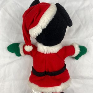 K&ouml;nnte beinhalten: Ein Pl&uuml;schtier im Weihnachtsmann-Outfit. Das Spielzeug hat einen schwarzen Kopf und Ohren, einen roten Weihnachtsmannhut mit wei&szlig;em Rand und einen roten Mantel mit schwarzem G&uuml;rtel. Die Handschuhe sind gr&uuml;n und der Mantel hat einen wei&szlig;en Rand.