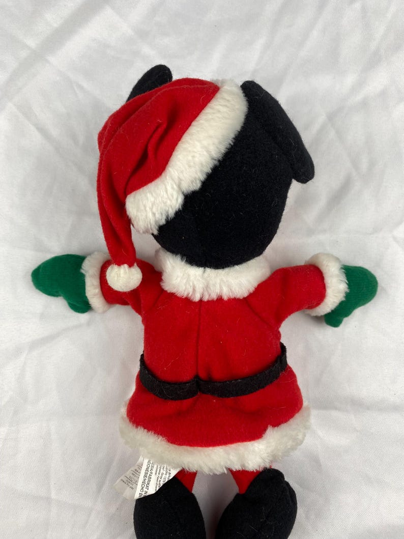 K&ouml;nnte beinhalten: Ein Pl&uuml;schtier im Weihnachtsmann-Outfit. Das Spielzeug hat einen schwarzen Kopf und Ohren, einen roten Weihnachtsmannhut mit wei&szlig;em Rand und einen roten Mantel mit schwarzem G&uuml;rtel. Die Handschuhe sind gr&uuml;n und der Mantel hat einen wei&szlig;en Rand.