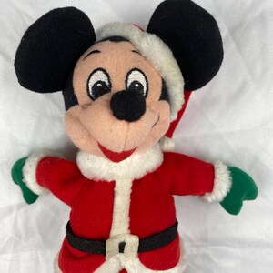 K&ouml;nnte beinhalten: Ein Mickey Mouse Pl&uuml;schtier im Weihnachtsmann-Outfit. Das Spielzeug hat schwarze Ohren, einen roten Weihnachtsmann-Anzug mit wei&szlig;em Besatz, einen schwarzen G&uuml;rtel und eine Weihnachtsm&uuml;tze. Die Handschuhe sind gr&uuml;n.