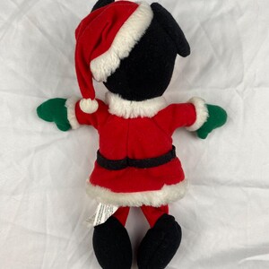 K&ouml;nnte beinhalten: Eine schwarze Pl&uuml;schfigur in einem roten Weihnachtsmann-Anzug mit wei&szlig;er Verzierung, passendem Hut und gr&uuml;nen Handschuhen. Die Figur hat schwarze F&uuml;&szlig;e und ist f&uuml;r die Weihnachtszeit gedacht.