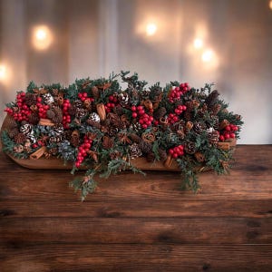 May include: A decorative centerpiece featuring a wooden bowl filled with green evergreen sprigs, brown pinecones, cinnamon sticks, star anise, and clusters of bright red berries. The arrangement is dense and textured, showcasing natural elements.