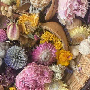May include: A woven basket filled with a variety of dried flowers in shades of pink, yellow, white, and purple. The arrangement includes peonies, daisies, and other floral elements, creating a colorful and textured display.