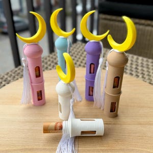 May include: Five colorful decorative towers with crescent moon tops and white tassels. The towers are made of plastic and have a clear window to see inside. One tower is white and has a bill inside.